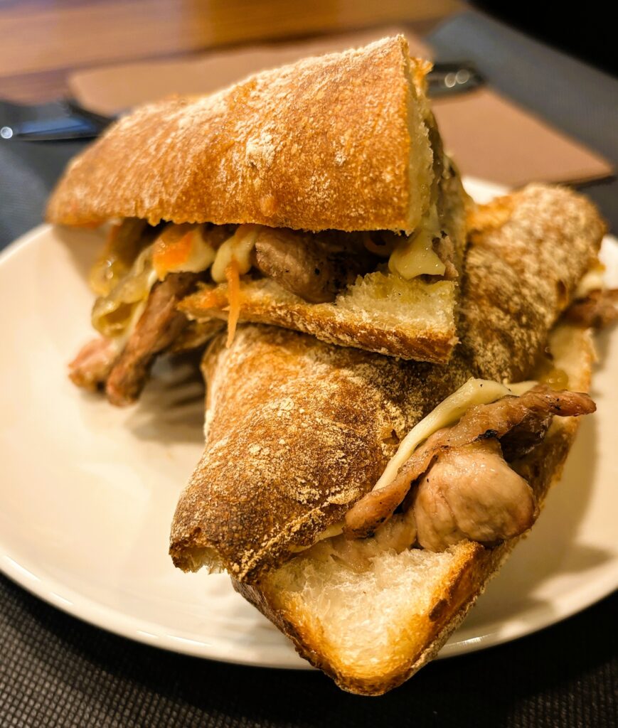 Al nou 180 Restaurant, al carrer Bonaventura Riberaygua, 24 d’Andorra la Vella, els entrepans i els esmorzars són gairebé una religió: amb un sol entrepà pots fer un esmorzar o un dinar com Déu mana. Des de primera hora del matí hi trobaràs un ambient de bar de tota la vida, amb entrepans generosos, producte de qualitat i aquella brasa que fa olor de bon esmorzar de forquilla. Els entrepans del 180 els pots encarregar clàssics o fets a la brasa amb carbó vegetal al forn Josper, perquè el pa surti lleugerament torrat i la carn amb aquell punt fumat tan especial. Pots combinar-los amb ceba confitada, formatge fos, bacó, truites, llom, botifarra o altres embotits, creant entrepans únics que no es troben fàcilment a Andorra la Vella. Són entrepans pensats perquè amb un sol bocí quedis ben servit: ideals per als qui comencen el dia amb gana, per als que fan una pausa ràpida a mig matí o per als qui volen dinar de pressa però amb menjar casolà i fet al moment. Sigui dret a la barra, assegut tranquil a taula o per emportar-se, els esmorzars i entrepans del 180 són el punt de trobada perfecte per carregar piles al centre d’Andorra la Vella. Al nou 180 Restaurant, al carrer Bonaventura Riberaygua, 24 d’Andorra la Vella, els entrepans i els esmorzars són gairebé una religió: amb un sol entrepà pots fer un esmorzar o un dinar com Déu mana. Des de primera hora del matí hi trobaràs un ambient de bar de tota la vida, amb entrepans generosos, producte de qualitat i aquella brasa que fa olor de bon esmorzar de forquilla.
Els entrepans del 180 els pots encarregar clàssics o fets a la brasa amb carbó vegetal al forn Josper, perquè el pa surti lleugerament torrat i la carn amb aquell punt fumat tan especial. Pots combinar-los amb ceba confitada, formatge fos, bacó, truites, llom, botifarra o altres embotits, creant entrepans únics que no es troben fàcilment a Andorra la Vella.
Són entrepans pensats perquè amb un sol bocí quedis ben servit: ideals per als qui comencen el dia amb gana, per als que fan una pausa ràpida a mig matí o per als qui volen dinar de pressa però amb menjar casolà i fet al moment. Sigui dret a la barra, assegut tranquil a taula o per emportar-se, els esmorzars i entrepans del 180 són el punt de trobada perfecte per carregar piles al centre d’Andorra la Vella.